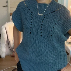 Blå stickad ärmlös tröja - Säljer en blå stickad tröja med grov virkning och snygga håldetaljer framtill. Tröjan är ärmlös med bred ribbad kant vid hals och nederdel, perfekt att styla över en långärmad topp eller t-shirt. Oversized och chill passform.