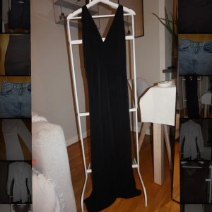 Svart långklänning med v-ringning - Elegant svart långklänning med djup v-ringning både fram och bak. Klänningen har smala axelband och ett stilrent, flytande fall. Perfekt för dig som vill ha en klassisk och tidlös look. Materialet känns mjukt och följsamt mot kroppen.