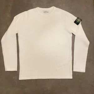 Vit stickad tröja från Stone Island - Vit stickad tröja från Stone Island med klassisk rund hals och lång ärm. Tröjan har den ikoniska Stone Island-loggan på vänster ärm, vilket ger en clean men ändå streetig vibe. Perfekt för dig som gillar stilrena plagg med tydlig branding.