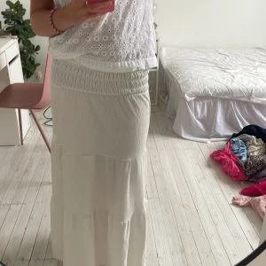 Vit långkjol från Gina Tricot - Supersöt vit långkjol från Gina Tricot med smock i midjan och volangdetaljer. Kjolen är luftig och har en lätt struktur i tyget, perfekt för varma dagar. Enkel att matcha med crop tops eller stickade tröjor. Fint skick. 