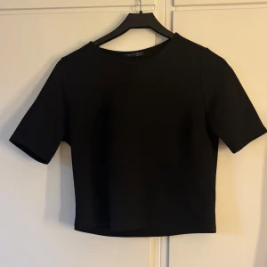 Svart topp från Atmosphere - En svart, kortärmad topp från Atmosphere i storlek 36. Toppen har en lätt strukturerad yta och rak passform med rund halsringning. Perfekt att styla med jeans eller kjol för en clean look. 