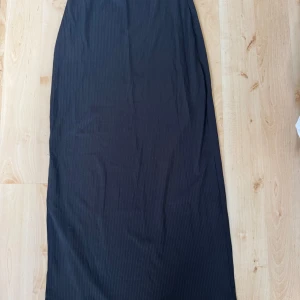 Svart långkjol med slits - Säljer en svart långkjol med slits på sidan. Kjolen har en rak och enkel passform som sitter snyggt i midjan och faller rakt ner. 
