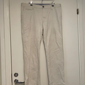 Beige chinos från Madison Avenue 34/30 - Snygga beige chinos från Madison Avenue, designade av KappAhl. Klassisk rak passform med bälteshällor, knapp och dragkedja i midjan samt diskreta fickor fram. Perfekta för en clean och stilren look.