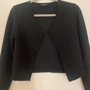 Svart cardigan jacka från ONLY - Svart cardigan jacka från ONLY i ribbad struktur. Jackan har öppen front utan knappar eller dragkedja och är långärmad. Enkel och stilren modell som är lätt att matcha till olika outfits.