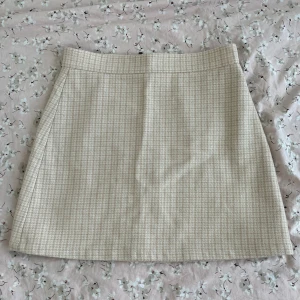 Beige rutig kjol från & Other Stories - Superfin beige kortkjol från & Other Stories med diskret rutigt mönster. Kjolen har en rak passform och dragkedja bak som snygg detalj. 