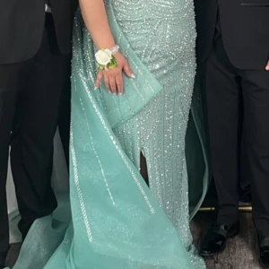 Ljusblå glittrig festklänning med slits - Magisk ljusblå långklänning med glittriga paljettdetaljer och vackert släp. Klänningen har figurnära passform, offshoulder och en snygg slits framtill. Perfekt för fester. Materialet känns lyxigt och skimrar i ljuset. Köpt från USA för 7000 kr. Pris kan diskuteras vid snabb affär. Använd endast i 3 timmar. 