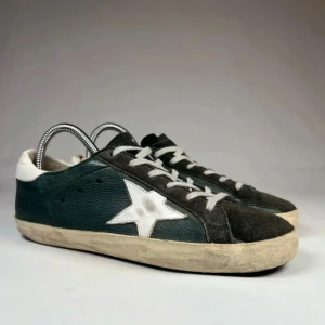 Golden goose sneakers - Snygga sneakers i svart och vitt med en stor vit stjärna på sidan. Ovandelen är i skinn och mocka, med vita snören och vit häl. Sulan är platt och har en vintage-look. Perfekta för dig som gillar streetstyle och vill sticka ut.