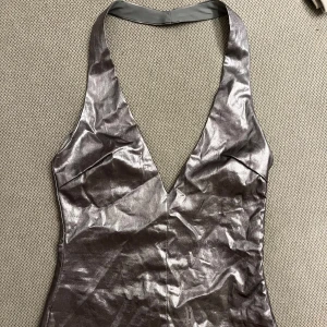 Silvrig halterneck topp från Zara - Supersnygg silvrig halterneck topp från Zara med djup v-ringning och glansig metallic finish. Aldrig använd 