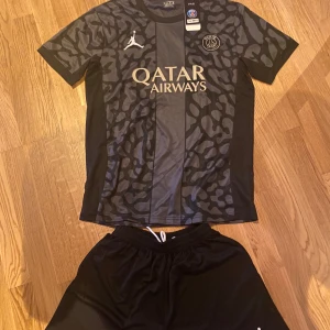 PSG x Jordan svart fotbollströja M, oanvända. - Snygg svart PSG fotbollströja i samarbete med Jordan. Tröjan har korta ärmar, coolt kamouflagemönster och Paris Saint-Germain-logga på bröstet. Tillverkad i lätt och ventilerande material, perfekt för match eller träning. Qatar Airways tryck på framsidan.