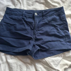 Mörkblå shorts med fickor - Snygga mörkblå shorts med  bälteshällor. De har en enkel knappstängning framtill och är perfekta för varma dagar. Modellen är midwaist och har en stilren look som passar till det mesta.