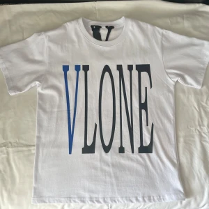 Vit VLONE t-shirt med blått tryck - Snygg vit t-shirt från VLONE med stort tryck i svart och blått framtill. På ryggen finns ett blått V med en detaljerad orm som slingrar sig runt bokstaven. Vanlig passform och tillverkad i 100% bomull. Perfekt statement-plagg för streetwear-stilen.