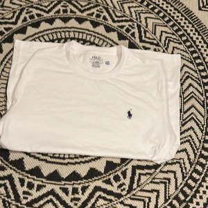 Vit t-shirt från Polo Ralph Lauren - Vit klassisk t-shirt från Polo Ralph Lauren med rund hals och liten mörkblå broderad logga på bröstet. Enkel och stilren modell i mjuk bomull, perfekt till jeans eller shorts. Endast testad. Tveka inte på att höra ev dig vid minsta fundering.