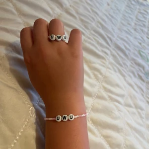 Sött pärlset med UWU-ring & armband - Supergulligt set med ett armband och en ring, båda med vita pärlor som stavar 'UWU' i svart. Armbandet har små ljusrosa pärlor runt om och ringen matchar med samma stil. Perfekt accessoar för dig som gillar kawaii och personliga smycken.