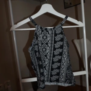 Svart och vit mönstrad linnetopp - Säljer en svart och vit linnetopp med tunna axelband och snyggt paisleyinspirerat mönster. Toppen har rak passform och är ärmlös, perfekt för varma dagar eller lager på lager. Mjuk och lätt i materialet, superenkel att styla till jeans eller kjol.
