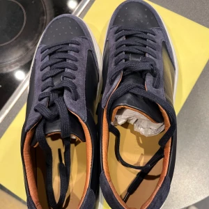 Svarta sneakers med bruna detaljer - Jag säljer mina J.lindeberg skor för att dom var för små när jag fick dom och gick inte att skicka tillbaks. Dom är helt helt nya och ny pris är 2000 kr och pris kan även diskuteras :)