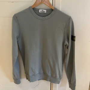 Grå tröja från Stone Island Junior - Säljer en stilren grå/ljusgrön tröja från Stone Island Junior. Tröjan har långa ärmar och en rund halsringning. Den ikoniska Stone Island-loggan sitter på ärmen. Perfekt för en avslappnad och trendig look. Storlek 12/156. Fint skick, använt ett fåtal gånger. Hör av dig för frågor :)