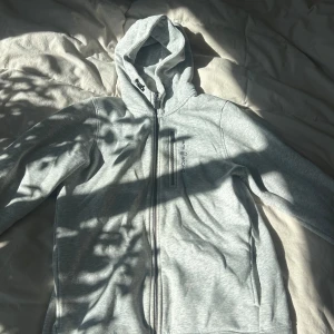 Grå huvtröja med dragkedja - Säljer en grå huvtröja med dragkedja framtill. Tröjan har långa ärmar och en bekväm huva. Perfekt för en avslappnad stil.användt 1 gång