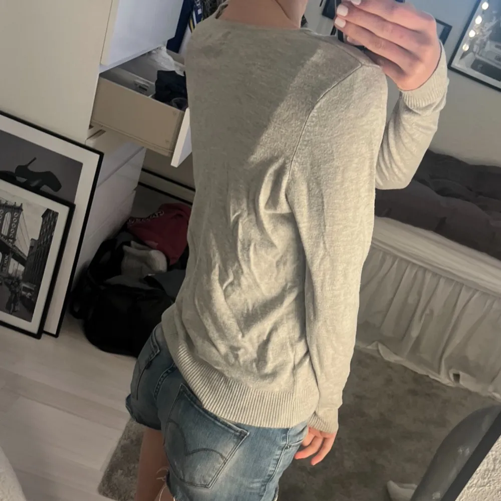 Säljer en stilren grå v-ringad tröja med långa ärmar. Tröjan har ribbade muddar vid ärmslut och nederkant, vilket ger en snygg passform. Perfekt för en avslappnad look.. Neuletakit & Villapaidat.