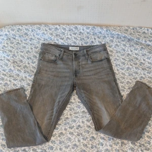 Grå jeansbyxor  - Snygga grå jeansbyxor med en klassisk femficksdesign. Byxorna har en dragkedja och knapp framtill. Perfekta för en avslappnad stil. Storlek 32/32 slim fit. 