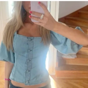 Ljusblå jeansblus med knappar - Snygg ljusblå jeansblus med knappar framtill och puffiga trekvartsärmar. Perfekt för en trendig look!