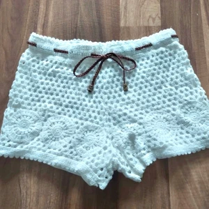 Vita virkade spetsshorts med knytband - Buda gärna🤍 Snygga vita virkade shorts med ett avtagbart brunt flätat knytband i midjan. Perfekta för en somrig look med sina detaljerade virkade mönster. Storlek xs - s