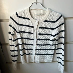 Vit och svart randig kofta från Primark - Säljer en snygg vit kofta med svarta ränder från Primark. Koftan har ett kabelstickat mönster och knäpps med knappar framtill. Står xs men passar även S då den är lite stor i storleken. Helt oanvänd 🌸