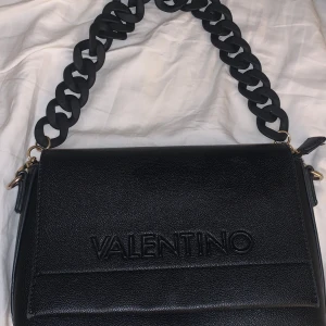 Svart väska från Valentino - Snygg svart axelväska från Valentino med ett brett axelband och ett kedjeband. Själva väskan ser helt oanvänd ut men insidan är såklart inte helt perfekt. Finns några små svarta fläckar på bandet men det är inte något man ser om man inte kollar riktigt noga💕💕 