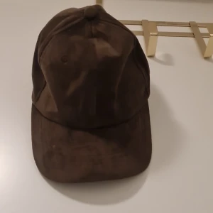 Brun keps - Snygg brun keps i ett mjukt material. Perfekt för en avslappnad stil. Justerbar rem baktill för bästa passform.