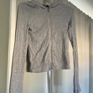 Grå huvtröja med dragkedja - Säljer en grå huvtröja från H&M med dragkedja framtill. Tröjan har en åtsittande passform och långa ärmar. Perfekt för en avslappnad stil.
