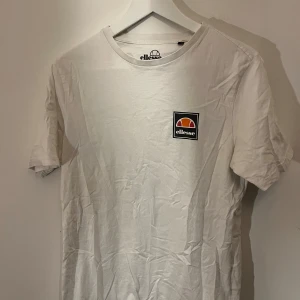 Vit t-shirt från Ellesse - Säljer en klassisk vit t-shirt från Ellesse med deras ikoniska logga på bröstet. T-shirten har en rund hals och korta ärmar, perfekt för en avslappnad stil.