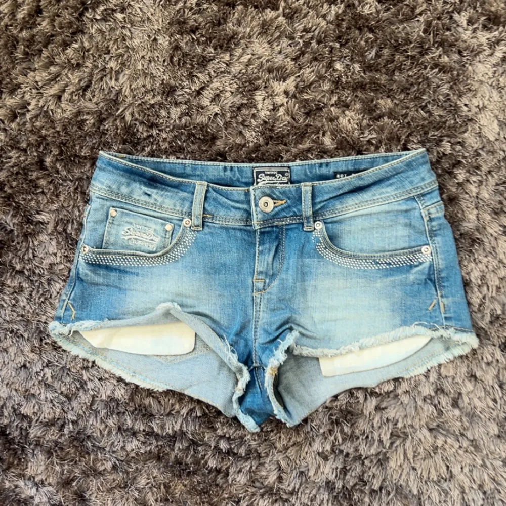 Säljer dessa jätte snygga lågmidjade jeansshorts från SuperDry vintage. Perfekta nu för sommarn!🌼Midja rakt över är 36cm!! Några små diamantpärlor har lossnat, men inget jag någonsin tänkt på! Hör av er vid frågor!!🤍🌼. Shortsit.