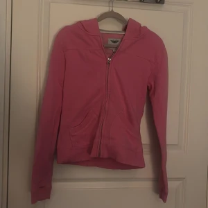 Rosa hoodie/tjock tröja från Grunt Girl - Säljer en rosa hoodie/tjock tröja från Grunt Girl med dragkedja och huva. Tröjan har långa ärmar. På baksidan finns texten 'Grunt Jeans' i ett dekorativt mönster. Perfekt för en avslappnad stil. Jätte fin!! Står storlek XL men den passar mer likt Small/Extra small!!!!!