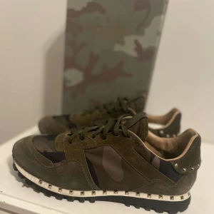Valentino Rockrunner i camouflage - Snygga Valentino Rockrunner sneakers i en cool camouflage-design. Skorna har en kombination av mocka och syntetmaterial med nitar runt hälen för en edgy look. Perfekta för dig som vill sticka ut!ingår förstås Box till skorna!(:
