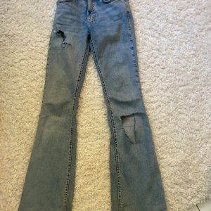 Blå jeans från Gina tricot  - Säljer ett par blå jeans från Gina tricot i storlek 32 med slitna detaljer på benen.  Använt mycket men de är i väldigt bra skick. 