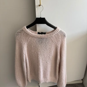 Ljusrosa/beige stickad tröja - Mysig ljusrosa/beige stickad tröja med en söt svart rosett där bak. Perfekt för kyliga dagar med sin mjuka och bekväma passform. Tröjan har långa ärmar och en rund halsringning. Nyskick aldrig använd 