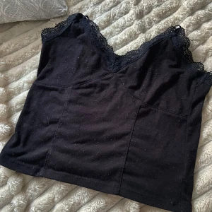 Svart linne med spetsdetaljer - Snygg svart linne med spetsdetaljer vid halsringningen. Perfekt för en stilren look. Linnet har en v-ringad design och ärmlös passform. Från h&m storlek xs.