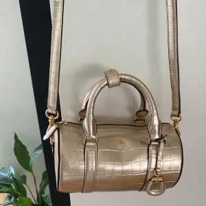 Guld axelväska från RL - Snygg guld väska från Ralph Lauren! Väskan har både handtag och en justerbar axelrem. 🩷priset kan diskuteras
