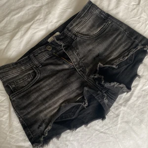 Svarta jeansshorts - Snygga svarta jeansshorts från H&M med fransiga kanter och slitna detaljer. Perfekta för en avslappnad stil. De har en klassisk femficksdesign och stängs med dragkedja och knapp. är stretchiga. Kontakta för mer info