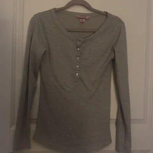 Grå långärmad tröja från Hunkemöller - Säljer en grå långärmad tröja från Hunkemöller. Tröjan har en knappdetalj framtill och är perfekt tröja att sova i. Den är tillverkad i ett mjukt material som känns skönt. 