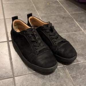 Svarta sneakers med röd sula - Snygga svarta sneakers med en iögonfallande röd sula. Skorna har snörning och en rund tå, vilket ger en klassisk look. Perfekta för en stilren vardagsstil.