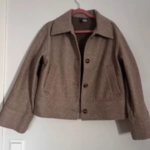 Beige kappa från H&M Divided - Säljer en stilren beige kappa från H&M Divided. Jackan har en klassisk krage och knäpps med knappar framtill. Den har långa ärmar och två fickor på sidorna. Perfekt för höst och vår!