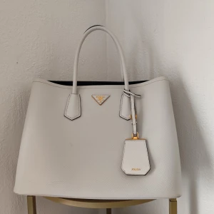 Prada saffino väska  - Elegant vit double saffino väska från Prada .Perfekt för att ge en lyxig touch till din outfit.  Nypris 48000 kr säljer för 15000 kr . Dustbag och certifikat/ äktenhetsbevis finns 