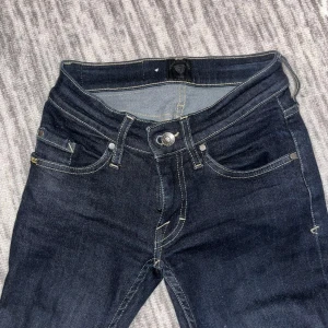 Mörkblå jeans från Tiger of Sweden - Snygga mörkblå jeans från Tiger of Sweden i modellen Slender. De har en klassisk femficksdesign och en knappgylf. Perfekta för en stilren look. Dom är low waist