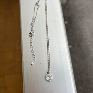 Silverfärgat halsband med glittrig berlock - Elegant silverfärgat halsband med en glittrig rund berlock. Perfekt för att lägga till en touch av glamour till din outfit. Kedjan är tunn och justerbar för att passa olika längder.