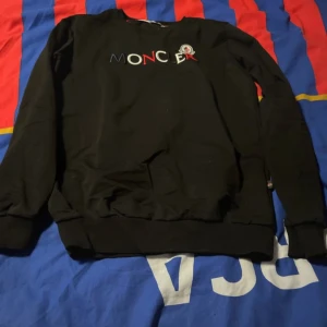 Svart tröja från Moncler - Säljer en svart tröja från Moncler med broderad logotyp på framsidan. Tröjan har långa ärmar och ribbade muddar vid ärmslut och nederkant. Perfekt för en stilren och bekväm look. Använd 1-2 gånger. Säljer pga att jag alldrig använder den.