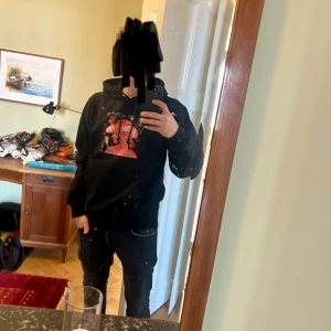 Svart hoodie med färgglatt tryck - Snygg svart hoodie med ett färgglatt och kreativt tryck på framsidan. Perfekt för en avslappnad stil med en touch av konstnärlig flair. Hoodien har en klassisk passform med långa ärmar och en praktisk magficka.