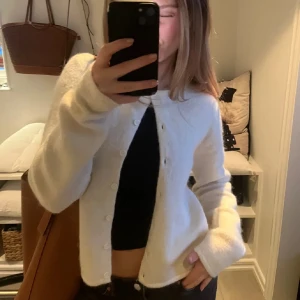 Vit kofta med knappar - Säljer en stilren vit kofta med knappar framtill. Perfekt för lager-på-lager och passar till många olika outfits. Koftan har långa ärmar och en klassisk design.