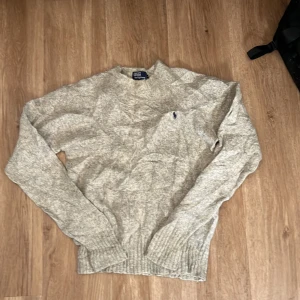 Grå stickad tröja från Polo Ralph Lauren - Säljer en stilren grå stickad tröja från Polo Ralph Lauren. Tröjan har en klassisk design med rund hals och ribbade muddar. Perfekt för kyligare dagar och ger en tidlös look.