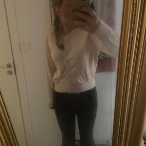 Ljusrosa kofta - Säljer en ljusrosa kofta med långa ärmar och knappar framtill. Perfekt för en stilren och bekväm look. Passar bra till både jeans och kjol. Går även att ha öppen, storlek L men jag på bilden har xs-s för en lite mer oversise look!