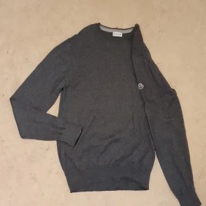 Grå tröja från Moncler - Säljer en stilren grå tröja från Moncler. Tröjan har en rund halsringning och ett diskret Moncler-märke på bröstet. Perfekt för en avslappnad men ändå elegant look.Det ni ser på bilden är det ni får😁 ett plagg som är köpt i bulk så jag vet lila lite som ni, men jag har kollat så gott jag kan på alla möjliga sajter och det jag kan kolla stämmer överens med originalet väldigt bra tröja raka o fina sömmar, kvalitets lappar och tyg